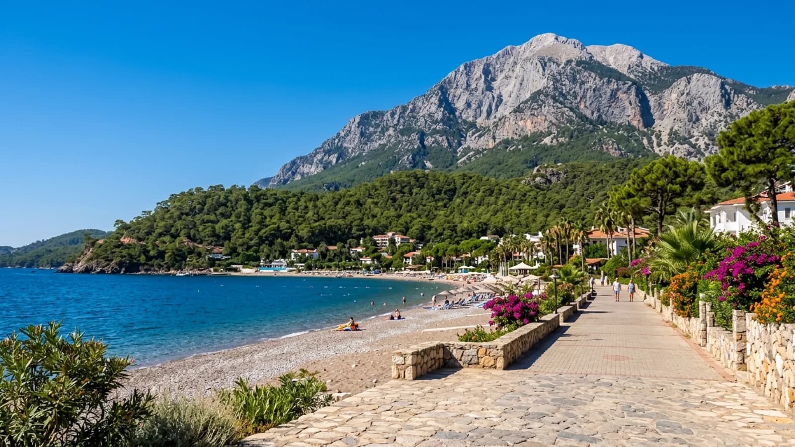 Het kiezelstrand van Tekirova met dichte dennenbossen, hoteltuinen en de oprijzende berg Tahtalı.