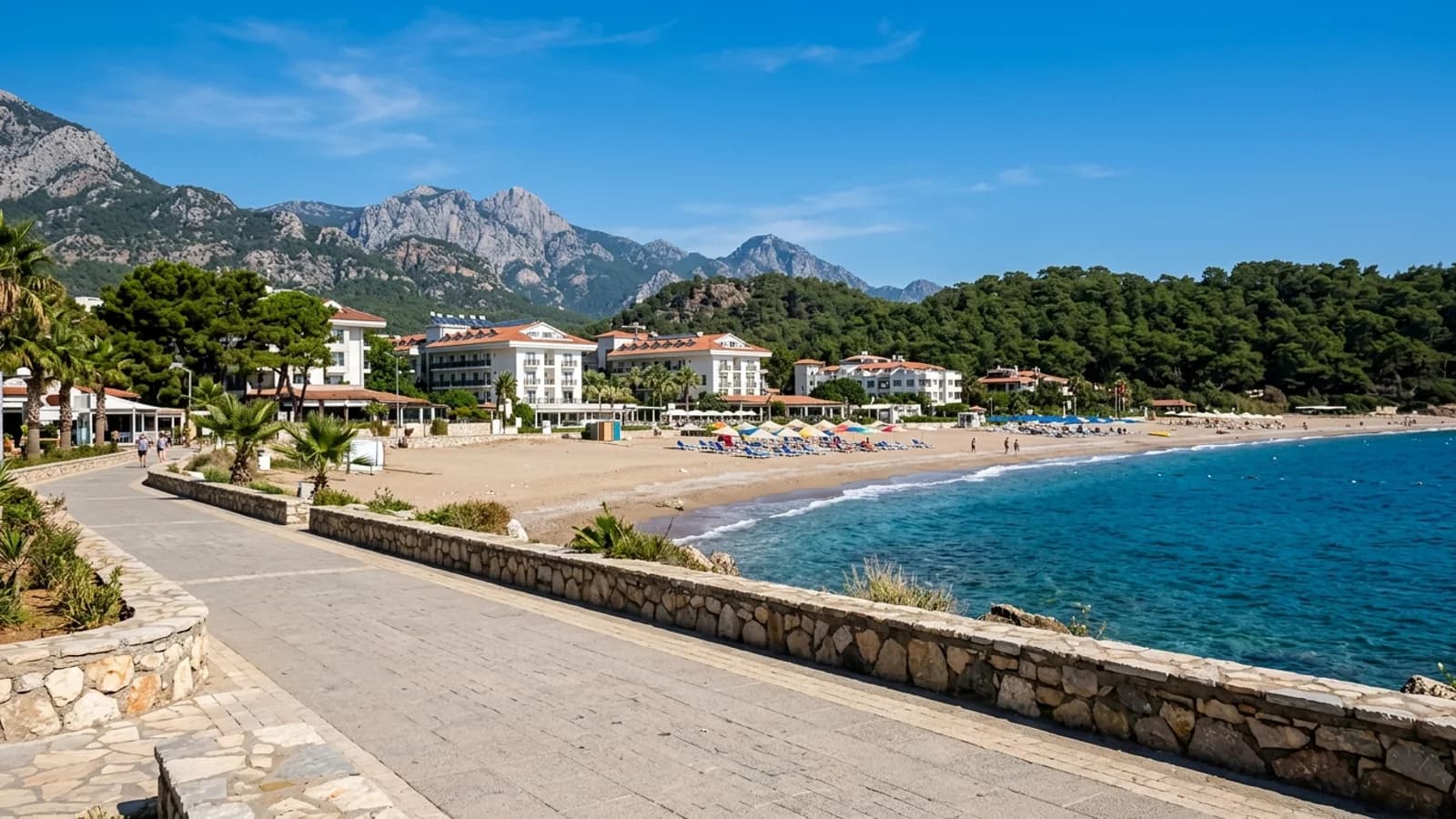 Çenger'deki kumsal plaj, arkasında çam ağaçları, resort oteller ve uzakta Toros Dağları'nın etekleri.