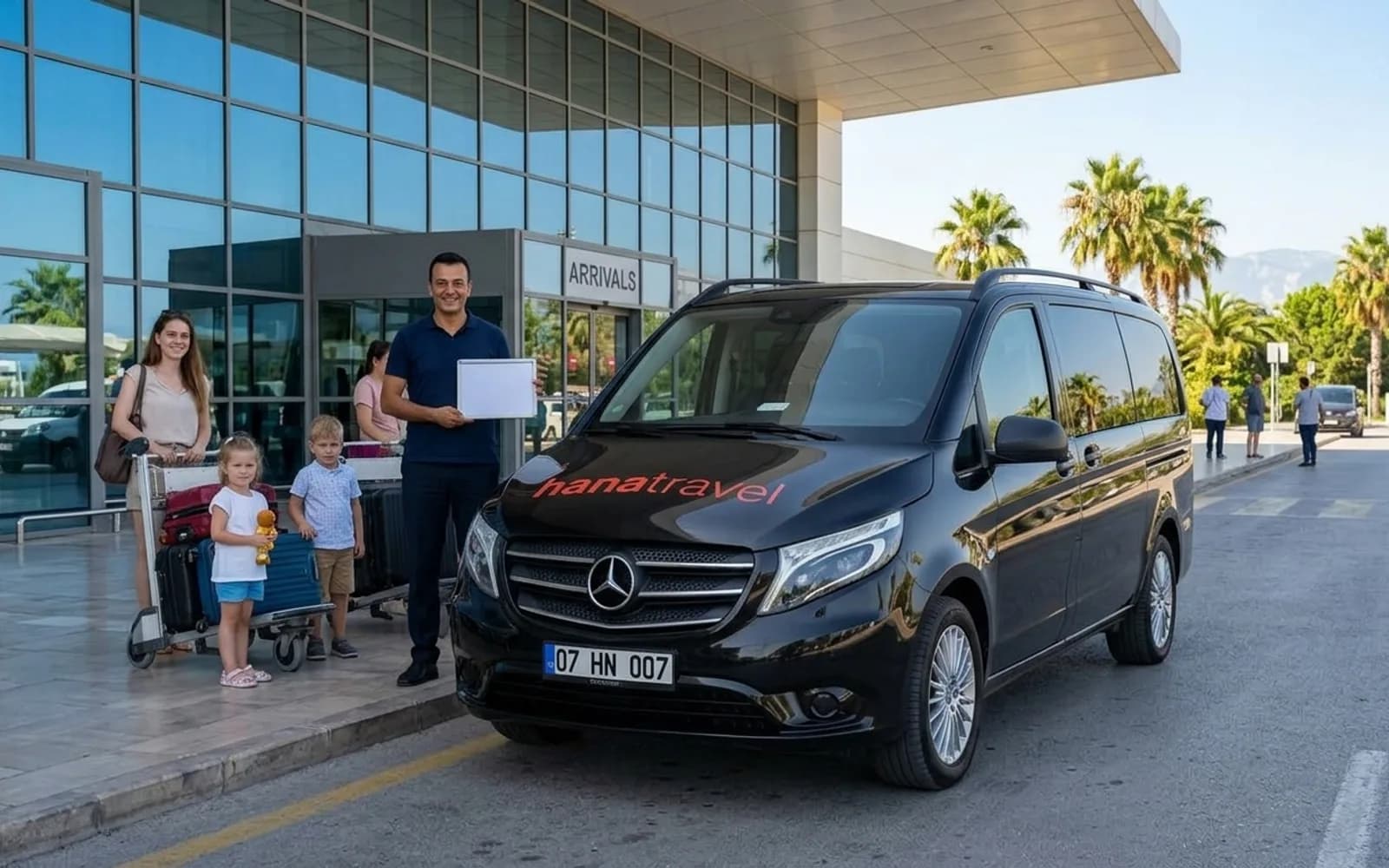 Ihr Name auf dem Schild, der Wagen am Bordstein Fahrer mit Namensschild begrüßt eine Familie neben dem schwarzen Hana Travel Vito vor der Ankunftshalle am Flughafen Antalya – Antalya Flughafentransfer
