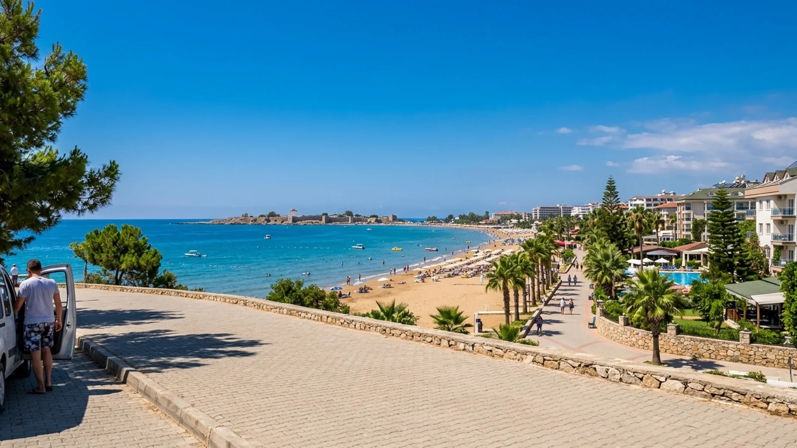 Kumköy beach with Side on the horizon Kumköy sandy beach with beachfront hotels, palm trees along a path and Side peninsula on the horizon.